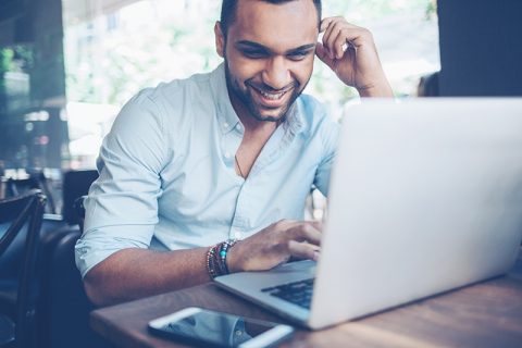 A man looking at his laptop's screen and smiling