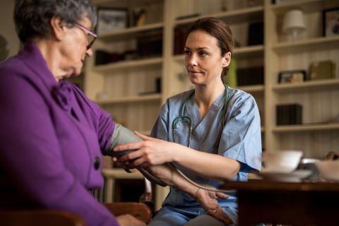 Young Caucasian female nurse taking a senior woman's blood pressure in a home library setting.