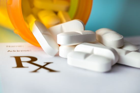 Prescription white pills spilling out of the bottle onto a blank prescription form on the table