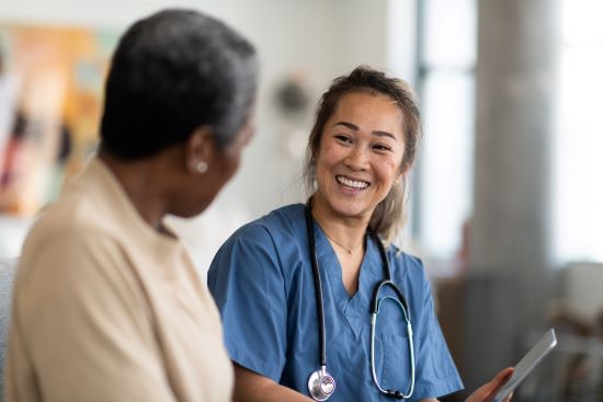 Female nurse and female patient having a conversation - The nurse wears a stethoscope around her neck and is holding a tablet computer