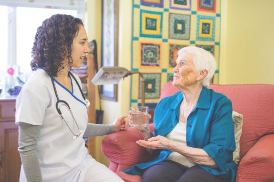 Young adult ethnic female nurse giving pills to elderly woman in nursing home facility