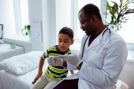 Male pediatrician showing curious boy a thermometer after measuring his body temperature.