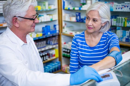 Male Pharmacist checking blood pressure of female customer in pharmacy