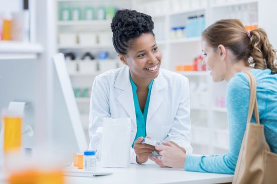 A Black female pharmacist provides medication instructions to a white female patient.