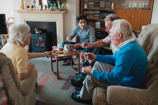 A teenage boy is assisting senior adults having tea at a nursing home.