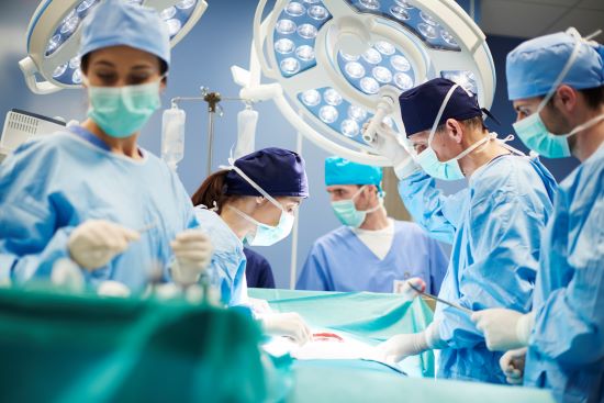 Un groupe de chirurgiens, hommes et femmes, dans une salle d'opération, en train d'opérer un patient qui a attendu longtemps pour être opéré.