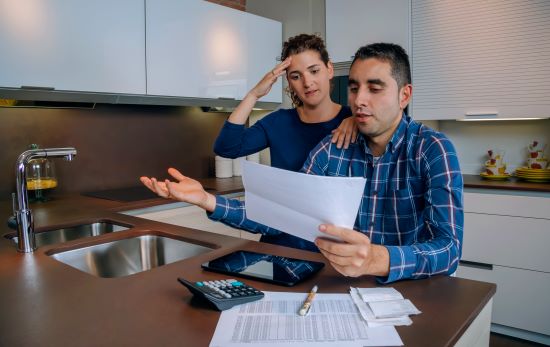 A young Hispanic couple are sitting at the kitchen counter reviewing their finances. The woman is clearly stressed by their financial situation. 
