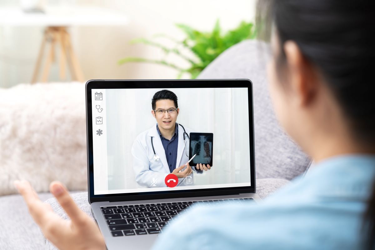 Une patiente est assise face à son écran d'ordinateur où son médecin décrit les résultats de son test lors d'un rendez-vous médical virtuel.