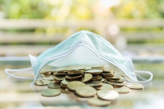 Pile of gold coins under a medical face mask to represent the high cost of health care related to COVID-19