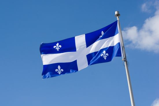 Quebec flag waving in a breeze set on a blue sky background with fluffy white clouds.