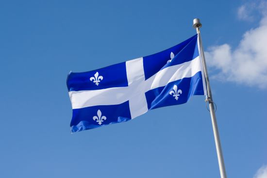 Quebec Flag blowing in a breeze on a blue sky background with fluffy white clouds.