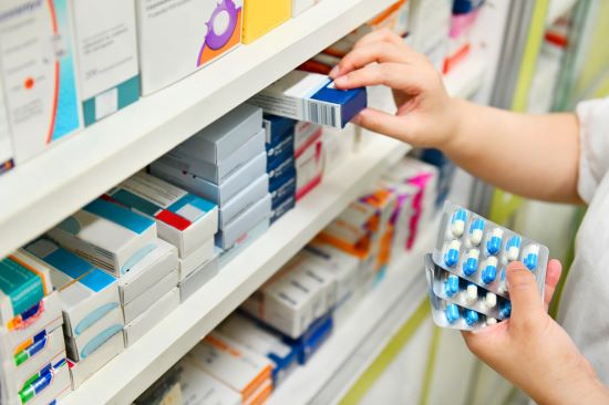 Image of a pharmacy shelf and a hand picking blister packs of pills off the shelf to fulfill a prescription.