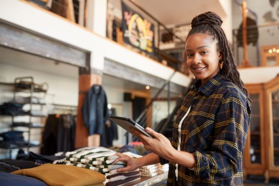 A smiling young Black female retail worker counting sweaters in a clothing store. 