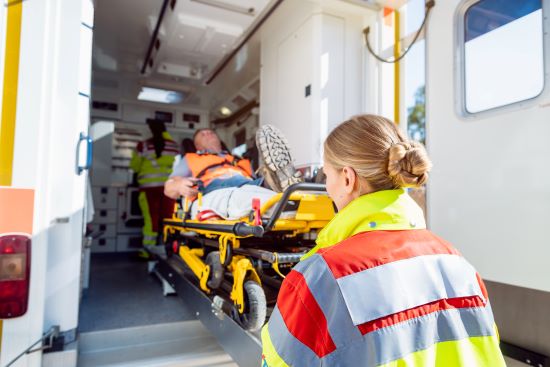 Paramedics in uniform putting injured man wearing a construction vest and work boots on stretcher into the ambulance.