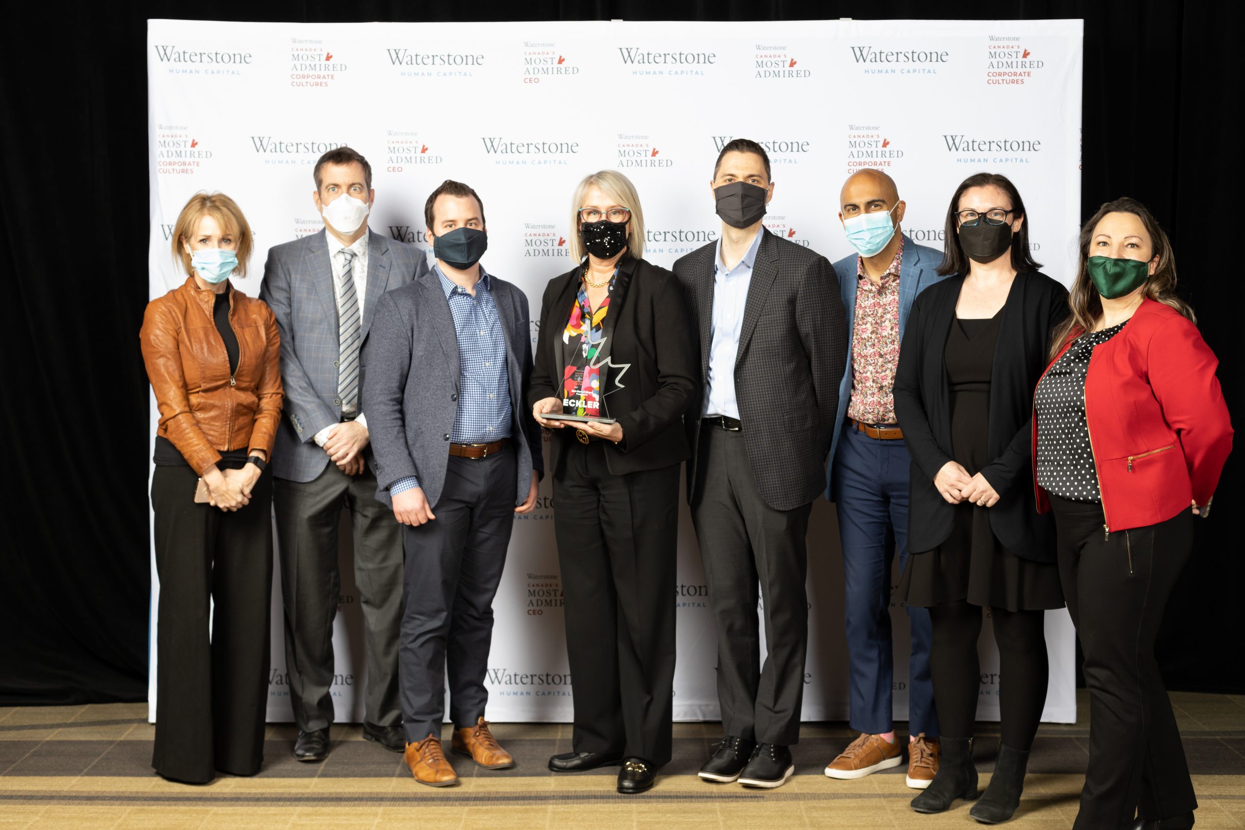 A group of Eckler consultants standing in front of a Waterstone Human Capital backdrop at the Canada's Most Admired Culture Awards gala. Jill Wagman, Eckler's Managing Principal, is in the centre holding Eckler's award.