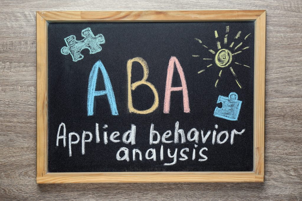 A small framed blackboard with text ABA Applied behavior analysis and drawings on wooden table, top view
