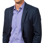 Photo of Eckler Johanan Schmuecker. He is wearing a black jacket and pants, with a light blue shirt and is looking straight into the camera smiling.