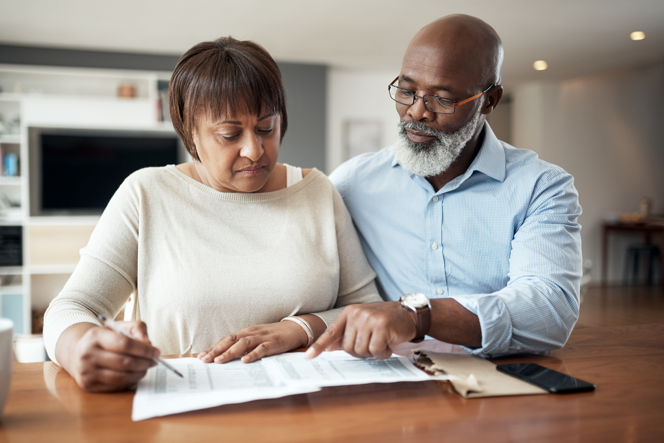 An older Black couple sitting at their dining table reviewing financial records to determine if they have enough income in retirement to cover their expenses.
