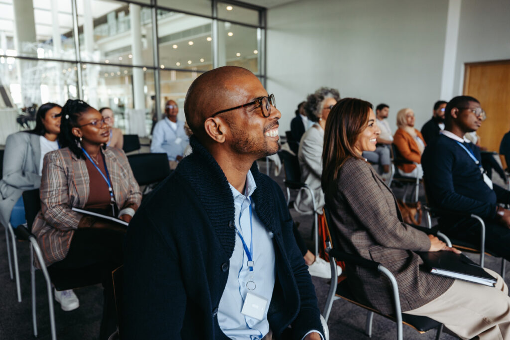 A professional male engaging in a presentation at a conference, with a diverse and attentive audience, showcasing focus and engagement.