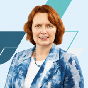 Studio headshot of Josephine wearing a blue patterned blazer and a beaded necklace, facing forward against a modern geometric blue and gray background.